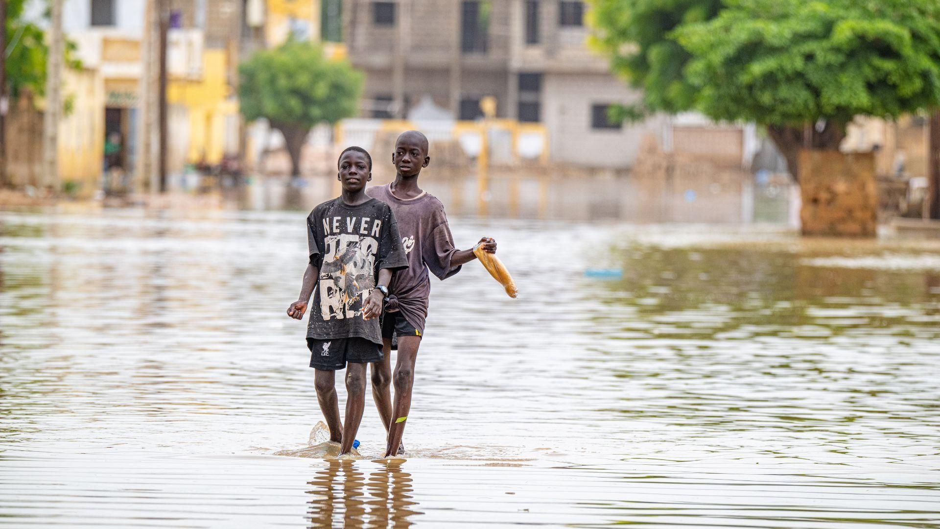 Two young children walking through a flooded urban street with waist-high water