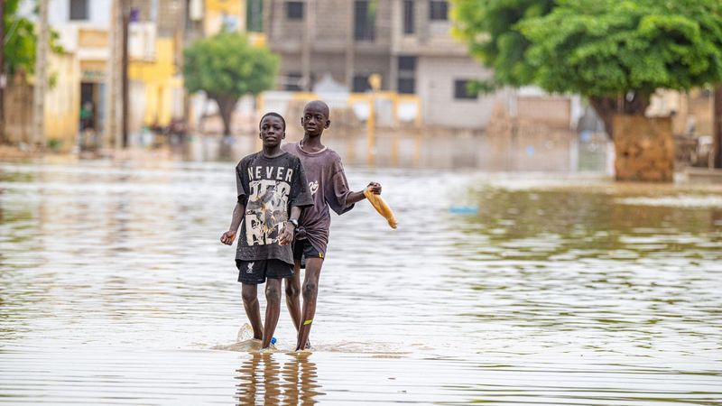 Two young children walking through a flooded urban street with waist-high water